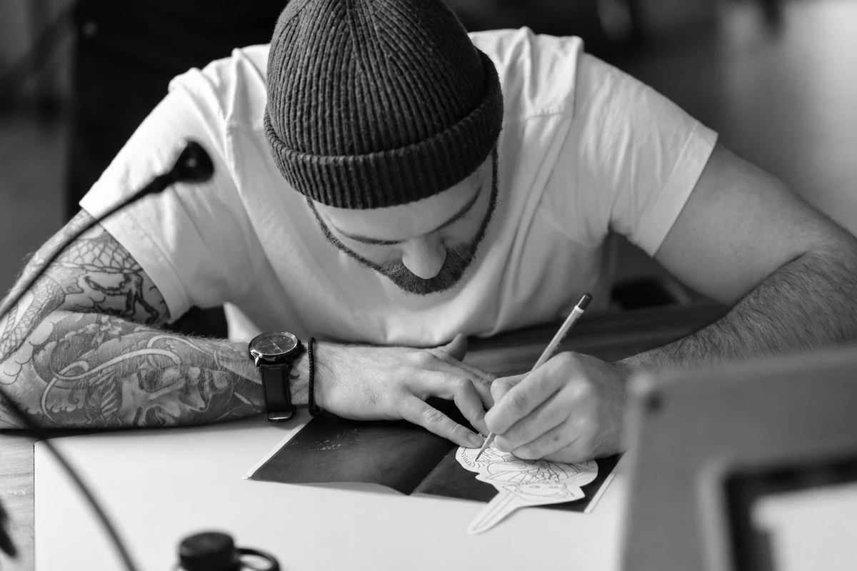 Artiste dessinant un motif de tatouage sur papier.