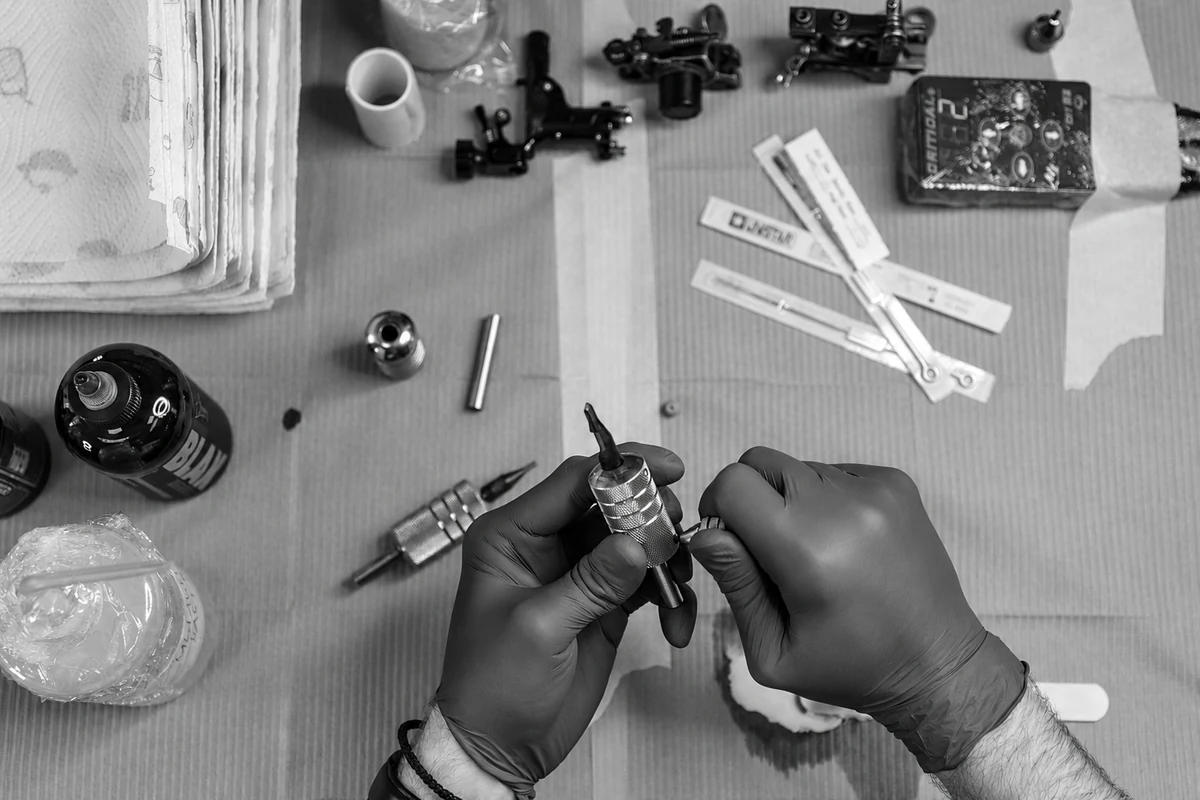 Mains gantées préparant une machine et du matériel de tatouage.