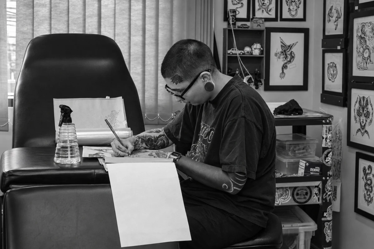 Atelier de tatouage avec un fauteuil, un poste de dessin et des flashs encadrés.