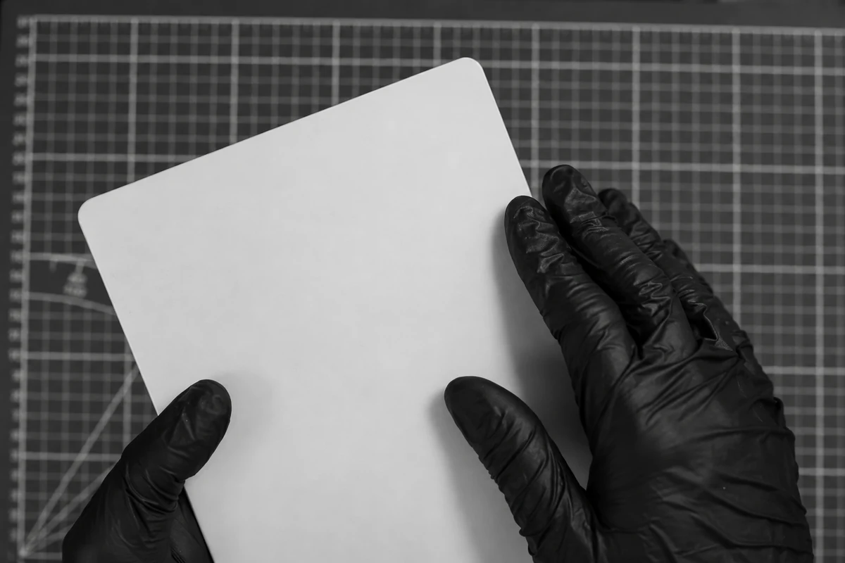 Mains gantées tenant une plaque vierge de peau synthétique.